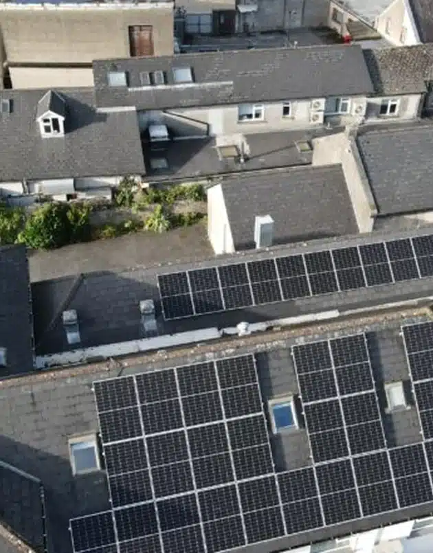 Aerial view of rooftops with solar panels installed on several buildings, surrounded by other buildings and greenery.